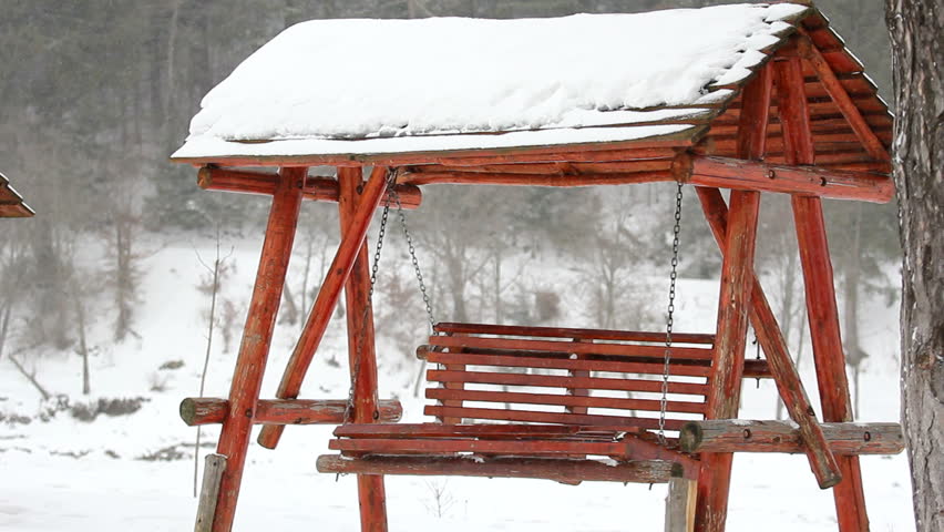 Empty wooden swing chair full of snow balancing
