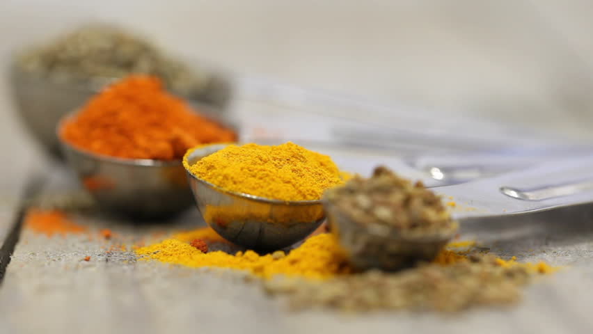 Various mixed spices (oregano, curcuma, paprika, anise) in metal scoops on wooden table