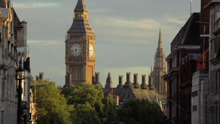 A stationary shot of Big Ben clock tower in London as seen from distance. There are houses and treetops. 