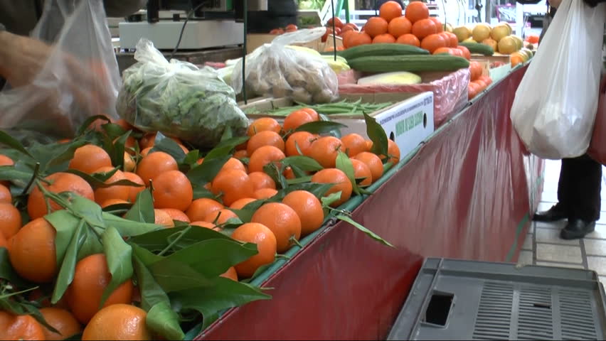 Farmers market vendor picks freshly grown oranges from bin, packs them in plastic bag for customer purchase. 1080p