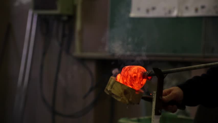 A glass blower is cooling molten glass in a factory.