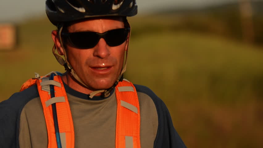 A mountain biker stops to take a drink of water from his pack as he rides a trail through a field during the day