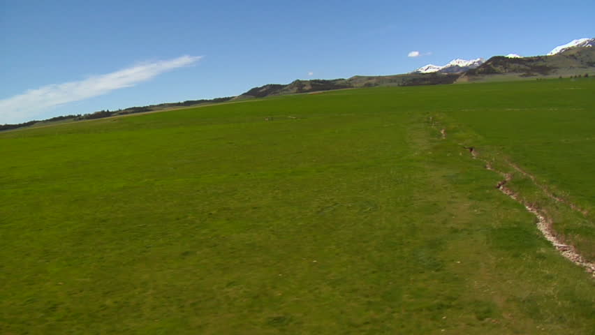 Wobbly aerial shot with green field and snow mountains in distance