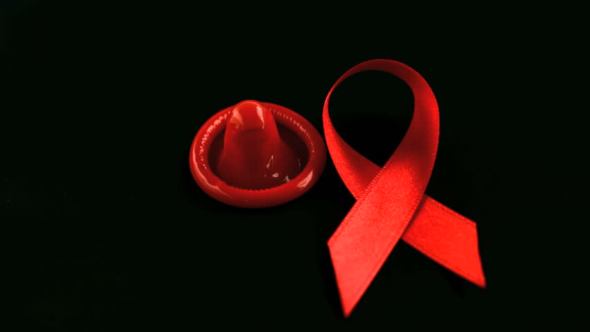 Aids red ribbon symbol falling down beside a condom in slow motion