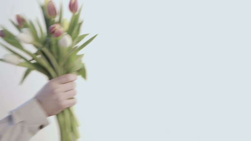 Man in beige shirt placing bunch of tulips in vase on pale blue background