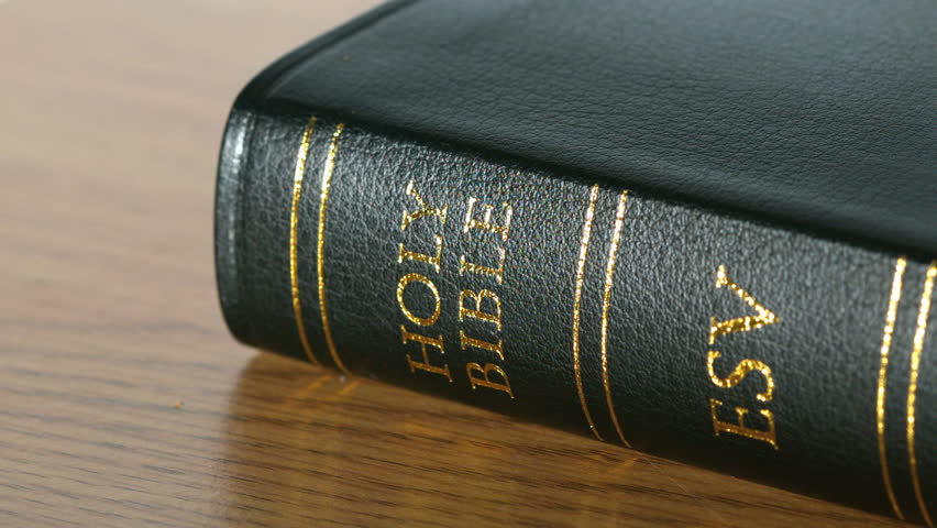 Rosary beads falling onto black bible in slow motion