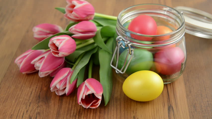 Rack focus on glass jar with bunch of pink tulips and Easter eggs
