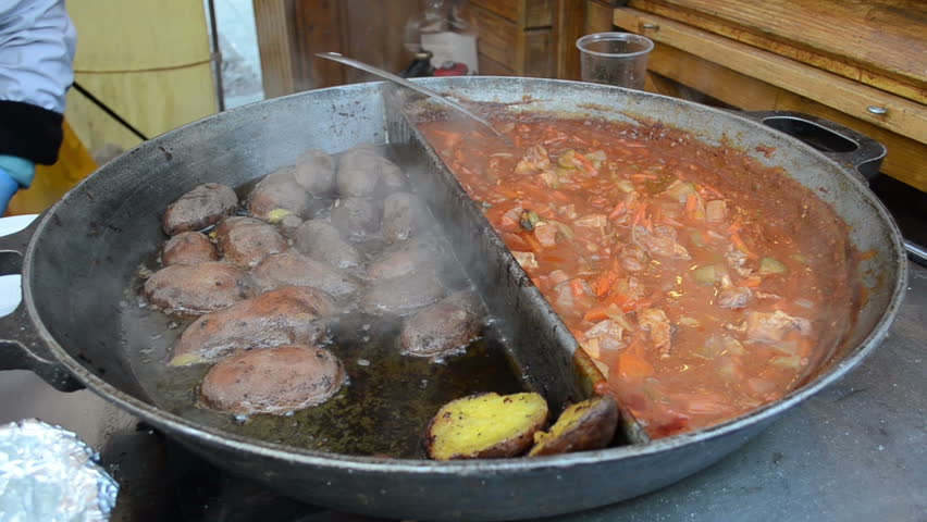 Potatoes vegetable meat stew and dumplings bake in huge steel pan in street outdoor restaurant.