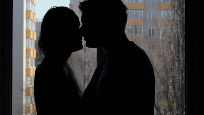 Two lovers embracing and kissing. Silhouette at the window.
