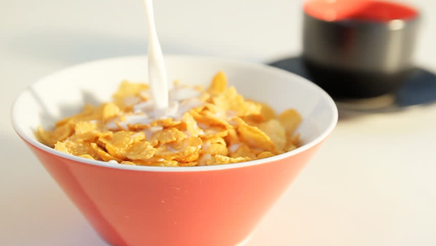 pouring corn flakes and milk inti a breakfast bowl with coffee cup in the background,shot taken with a wide aperture shallow dof