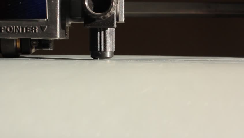 Cutting plotters use knives to cut the letters on gray vinyl film. Close-up view from below