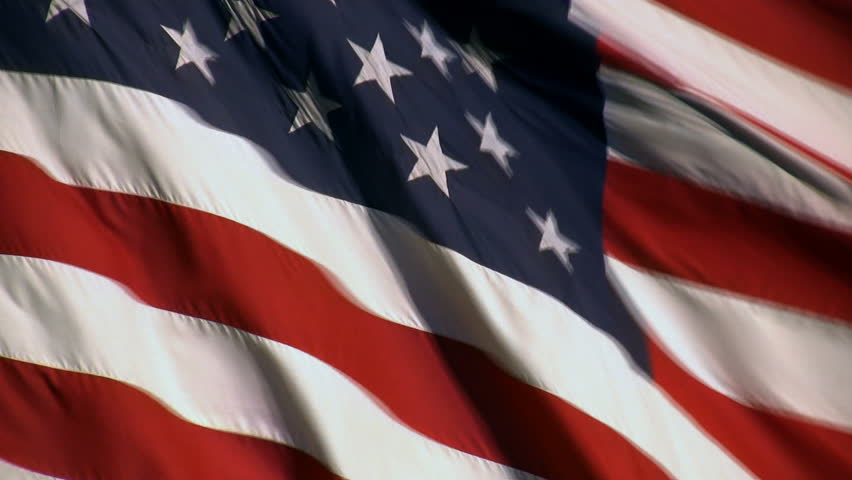 A real American Flag waving. Some blue sky shows through at times.