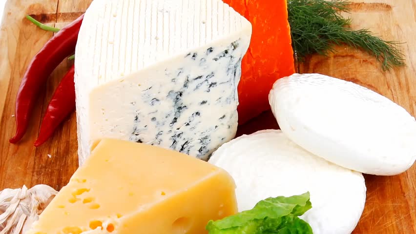 several delicatessen types of cheese on wooden board with hot peppers and dill isolated on white background