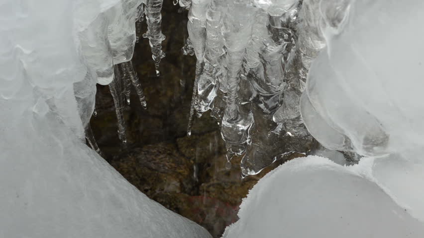ice and icicles flow melt water drop on stones in mountain cave.