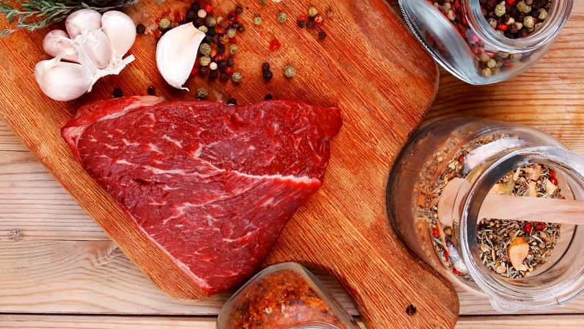 fresh raw beef meat fillet flesh with peppercorn and thyme ready to grill on wood figured old style board over table with spices in glass
