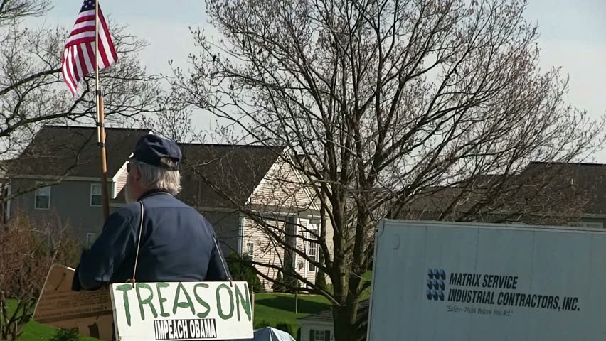 EPHRATA, PENNSYLVANIA - APRIL 17: Man in revolutionary war outfit carrying 'Impeach Obama' protest sign and American flag on April 17, 2013 in Ephrata, Pennsylvania.