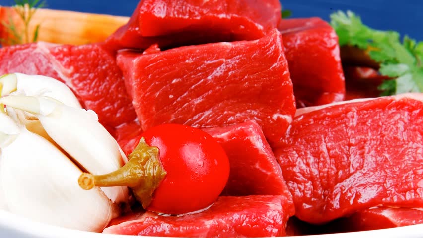 slices of raw fresh beef meat fillet in a white bowls with dill and green peppers serving over blue wooden table