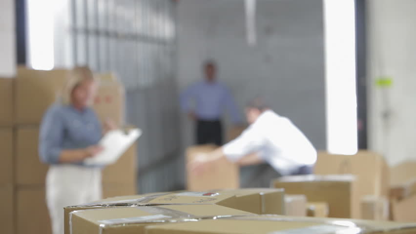 Shallow focus view of workers taking boxes from conveyor belt as they are checked by woman with clipboard.Shot on Canon 5d Mk2 with a frame rate of 30fps
