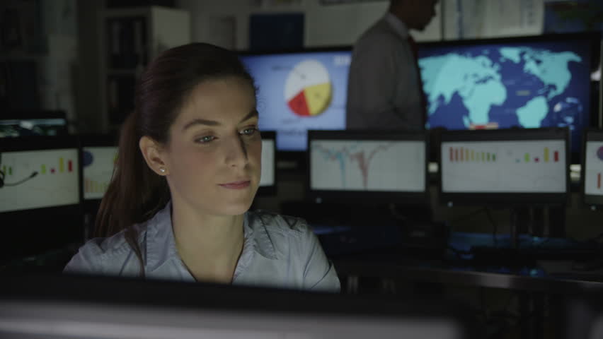 A young business woman is working late at night in a dark office filled with computer screens. She is feeling tired and overworked. In slow motion.