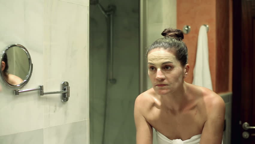 Young woman washing off face mask in front of mirror

