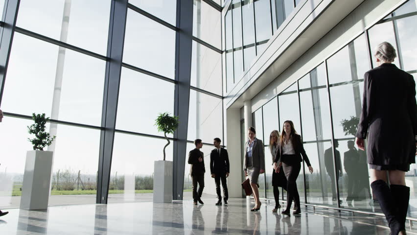 Three businessmen meet and shake hands in a busy modern office building on a bright day. In slow motion.
