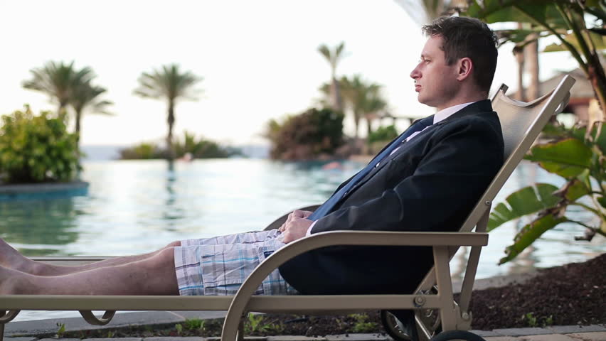 Happy businessman relaxing on sunbed by the pool
