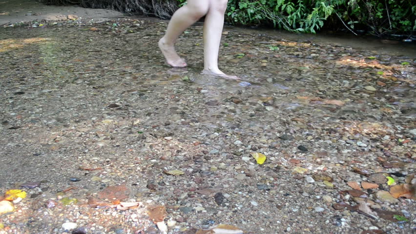 woman legs painted red foot nails walk through park forest stream brook water flow.