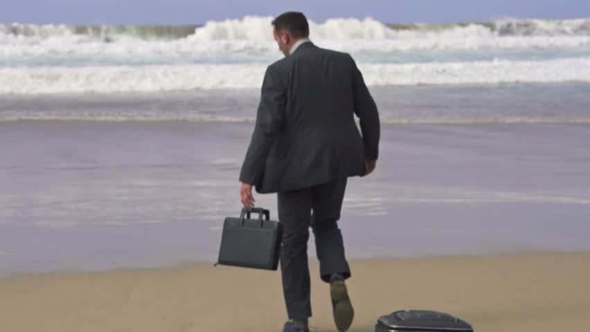Businessman with suitcase walking on beach
