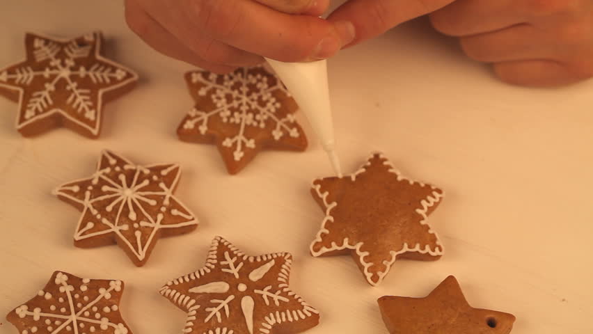 Close-up of hand with pipping bag decorating gingerbread cookies.