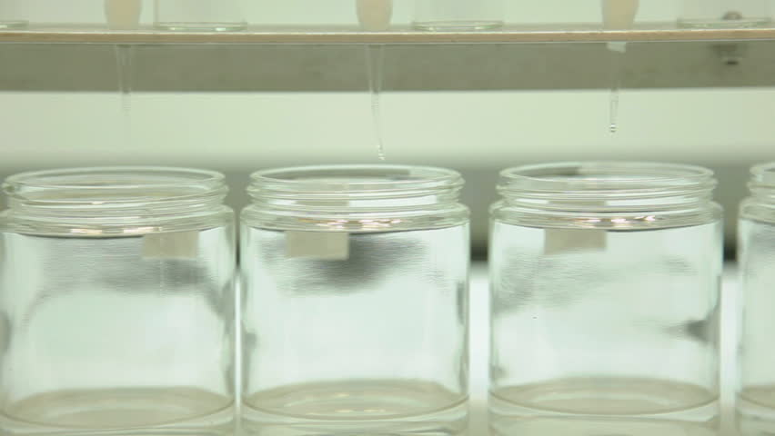 A slider (dolly) shot in a chemistry laboratory moving past a row of glass beakers that are collecting a clear liquid.