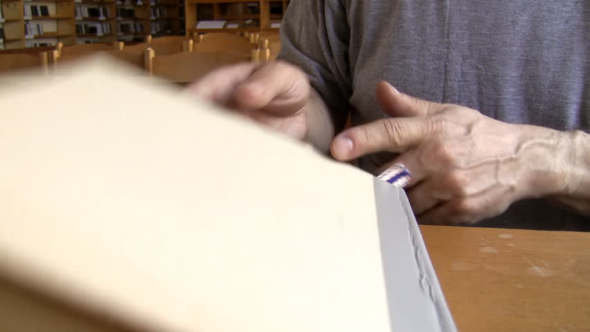 While sitting man closes a book with blank cover stands up and goes away leaving empty chairs, tables and bookshelves behind