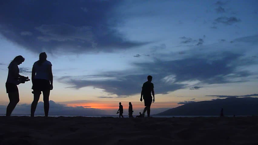 Unrecognizable people enjoying the evening sunset at the beach in Hawaii.