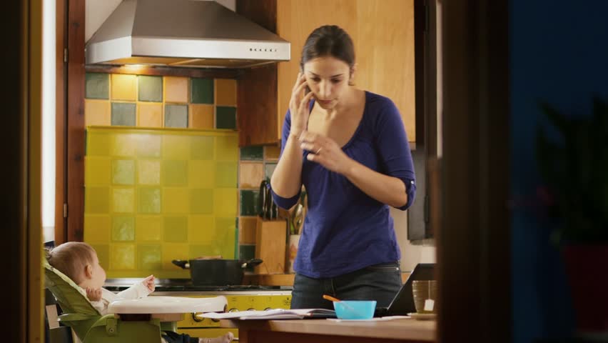 Busy businesswoman with telephone, multitasking mother cooking and working, feeding baby girl at home