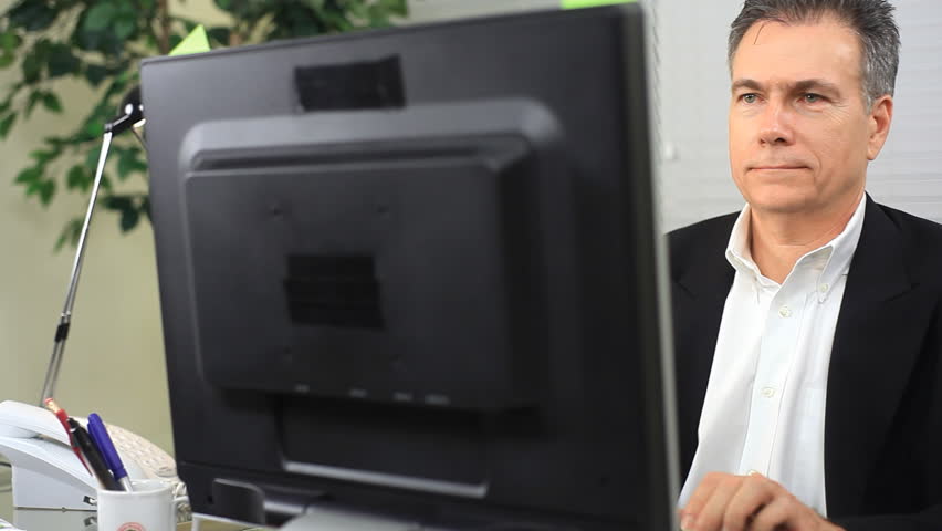 A pleased businessman sittingin his office working at his computer.