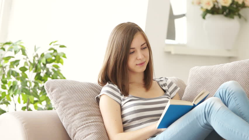 Young woman reading book and looking out the window

