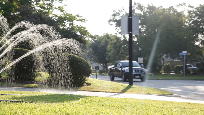 A water sprinkler watering a parched front lawn on a hot Southern summer morning.