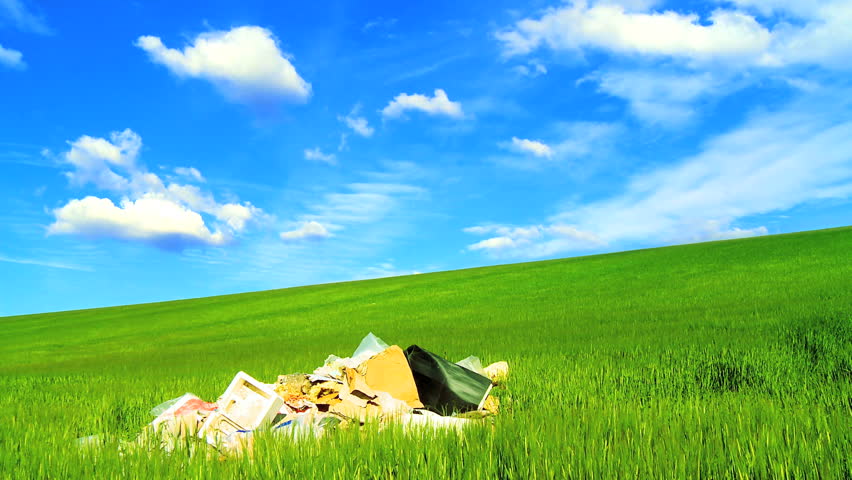 Concept shot of rubbish (trash) polluting a clean environmental field under t/lapse clouds on a loop