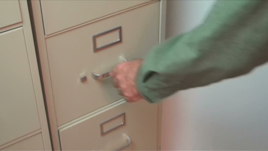 Businessman removes folders from company office filing cabinet drawer.