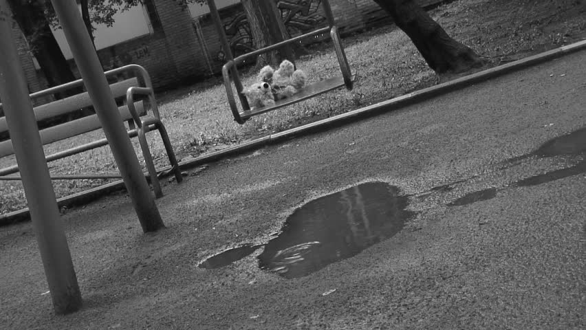 Forgotten Teddy bear on a swing under rain. Deep depression theme. Black and white.