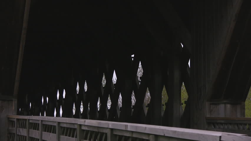 Closeup of an empty wooden covered walking bridge, zooming out to reveal the foliage that surrounds it.  Located in Guelph, Ontario, Canada