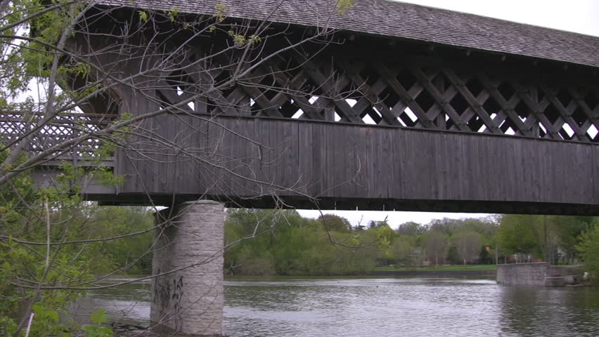 A pan along the length of a wooden covered walking bridge, shot from the river below.  Guelph, Ontario, Canada