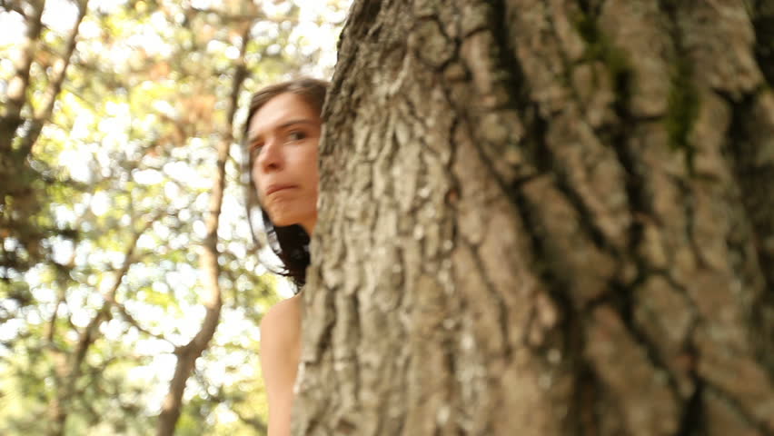 Young woman hide and seek behind a tree.