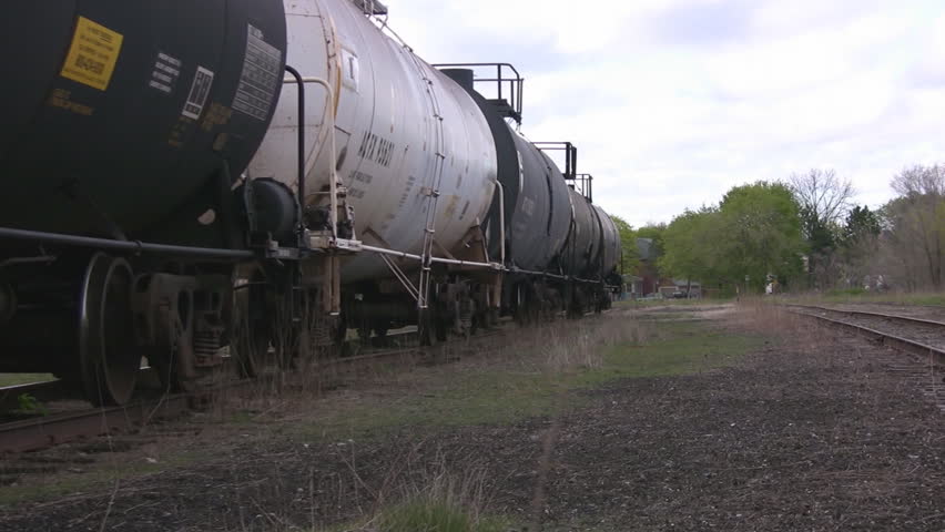 A zoom out along the railroad tracks, highlighting a line of industrial tankers at rest.