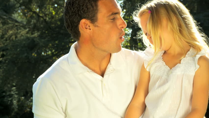 Young father tenderly holding his daughter while outdoors on a summers day