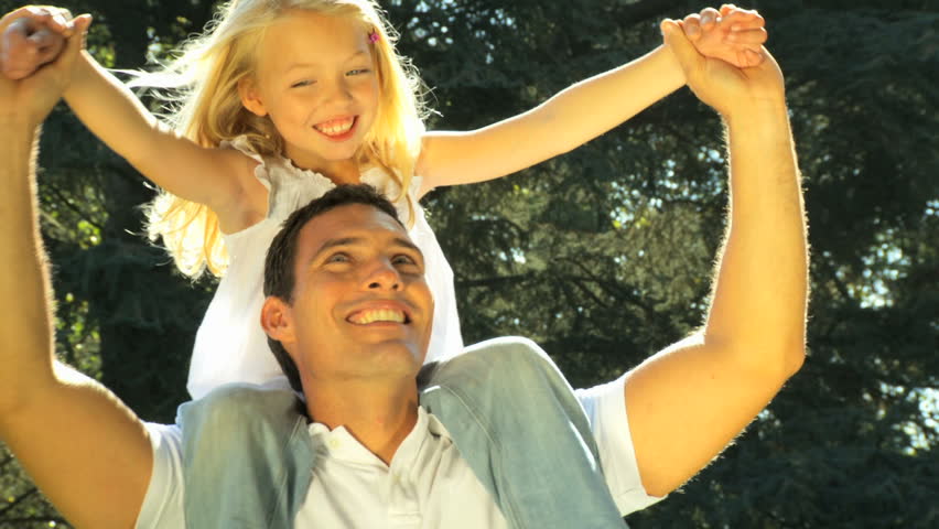 Young father laughing with his daughter on his shoulders while outdoors on a summers day