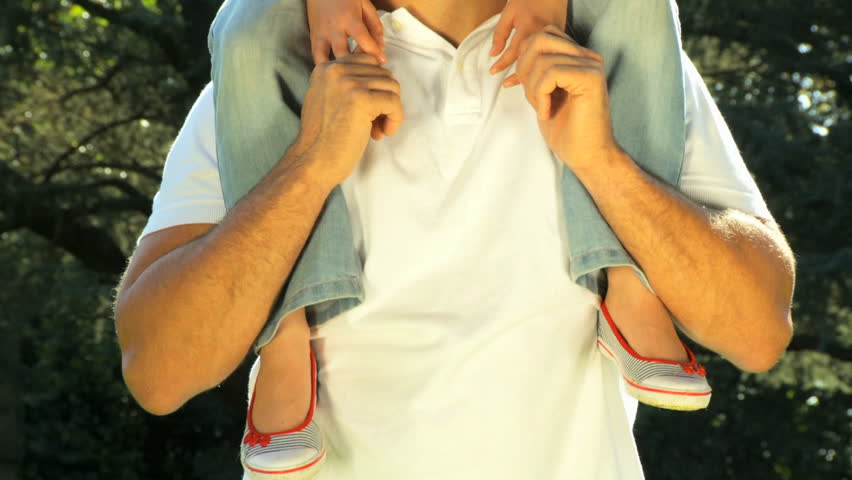 Young father tenderly holding his daughter on his shoulders while outdoors on a summers day