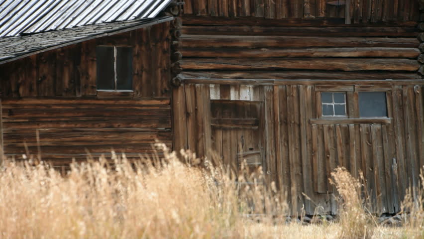 Close up of old wood log barn in the valley meadow Grand Teton National Park Wyoming. Grass blowing in wind. Trail to front doors. Clouds cover peaks of the mountains. Pioneer building on Mormon Row.
