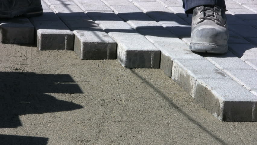 A worker patiently installs interlocking sidewalk bricks on a sunny day. 