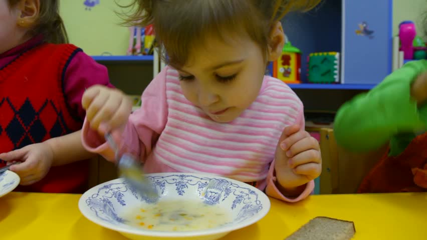 Little girl eating porridge in the kindergarten 