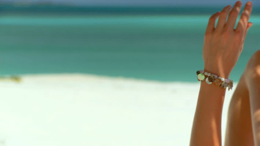 Elegant young female relaxing on white sandy beach looking at aquamarine waters